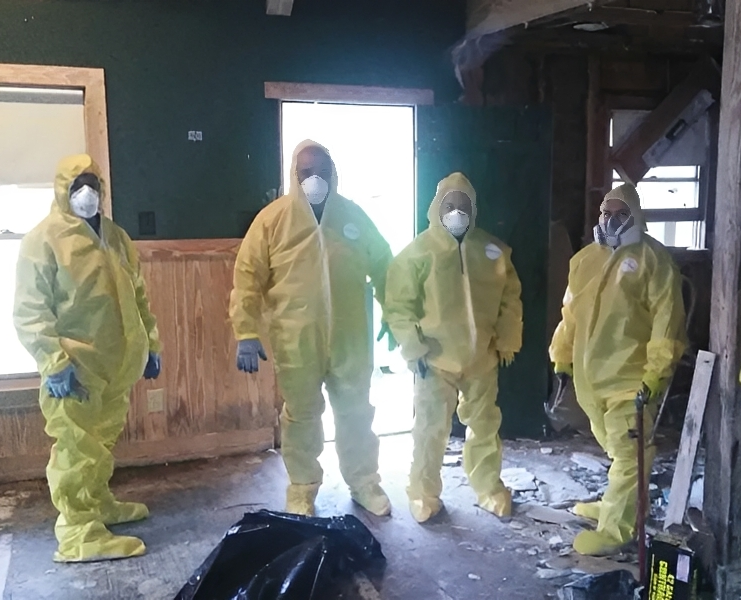 Four people in hazmat suits indoors.