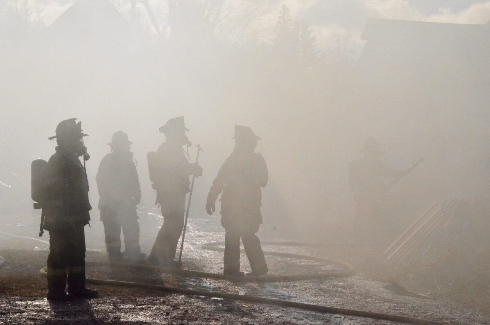 Firefighters standing in heavy smoke outdoors.