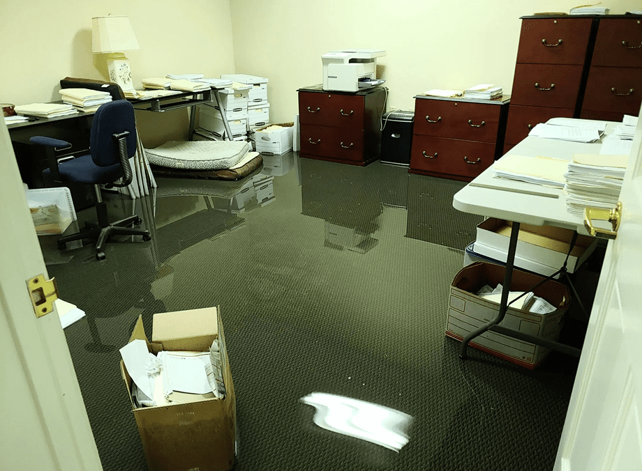 Flooded office with scattered papers and furniture.